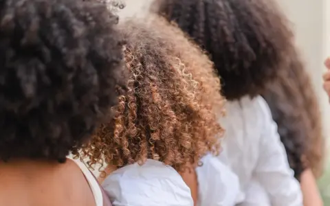 Trois femmes avec de magnifiques cheveux frisés, un mélange de bruns foncés et de châtain clair, se tiennent côte à côte.