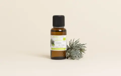 Flacon d'huile essentielle de cèdre de l'Atlas, aux vertus purifiantes et calmantes, posé à côté d'une branche de cèdre.