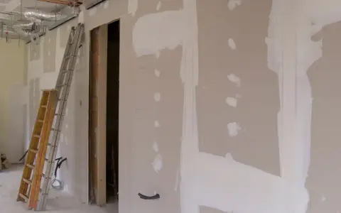 Scianka dzialowa z plyty kartonowo gipsowej w trakcie prac. Widoczne drabiny, instalacje i otwór drzwiowy.