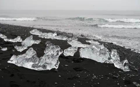 Lodowe bryły na czarnym piasku tworzą magiczną diamentową plażę Islandii. Fale oceanu delikatnie obmywają ten niezwykły krajobraz.