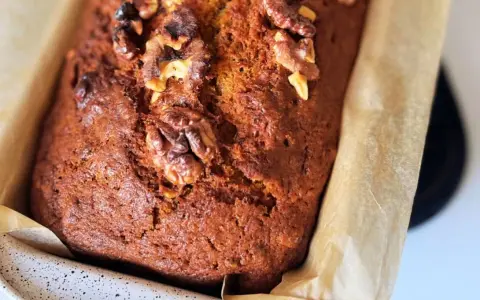 Szybkie i tanie ciasto marchewkowe z orzechami włoskimi, upieczone w keksówce wyłożonej papierem.