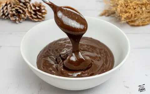 Cuchara con ganache de chocolate cayendo en un cuenco blanco. El chocolate es brillante y sedoso, perfecto para postres.