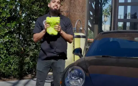 Man holding a fluffy wash mitt, ready to demonstrate how to wash a convertible car.