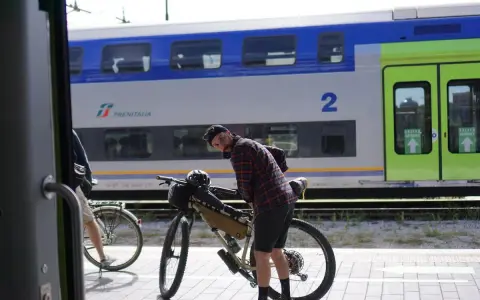 Ciclista con bici da gravel alla stazione, pronto per il viaggio da Rimini a Bellaria. Il treno Trenitalia è sullo sfondo.