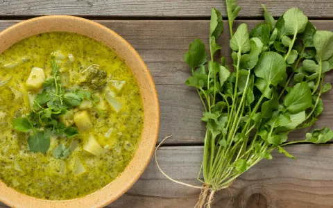Soupe crémeuse aux pommes de terre et au cresson de para frais, garnie de feuilles vertes.