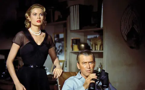Grace Kelly e James Stewart in una scena di un film thriller suspense. Lui osserva con il binocolo, lei elegante in abito nero.