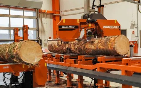 Pomarańczowa maszyna do obróbki drewna Wood-Mizer WM2500 przetwarza pień drzewa na deski.