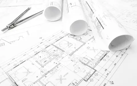 Projekt budowlany domu z widocznym cyrklem i zwiniętymi planami.