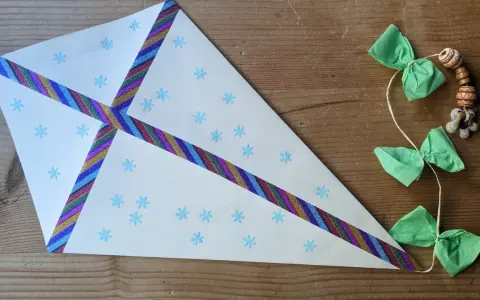 Ein selbstgebastelter Drachen mit Schneeflocken und bunten Bändern, perfekt für basteln mit Kindern ab 7 Jahre. Daneben eine Schnur mit grünen Schleifen und Holzperlen.