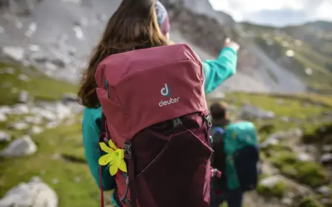 Dwie osoby w górach, jedna z plecakiem Deuter, wskazująca drogę.