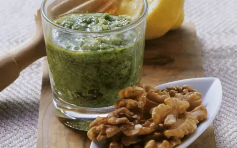 Frisches Petersilienpesto im Glas, daneben Walnüsse und eine Zitronenhälfte. Perfekt für Petersilie Rezepte.