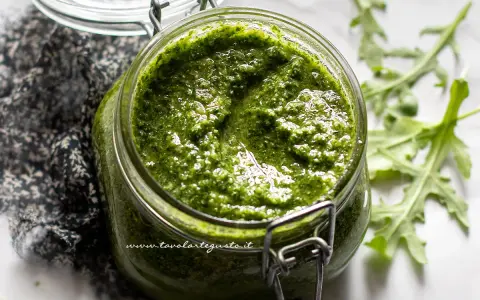 Un vasetto di pesto di rucola fatto in casa, con foglie di rucola fresca sullo sfondo.