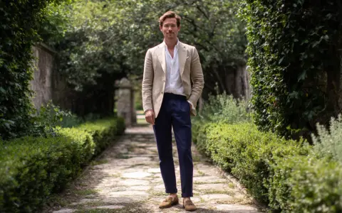 Uomo con giacca beige e pantaloni blu, un look che evoca un raffinato stile francese.