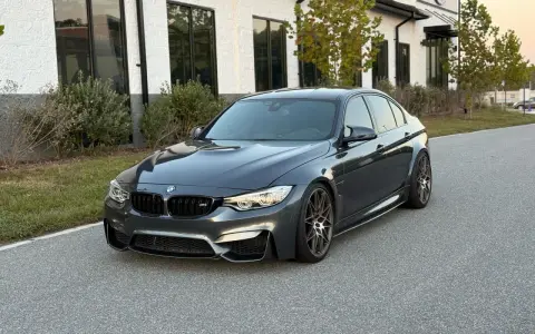 Szary sedan BMW M3 na tle nowoczesnego budynku. Sprawdź aktualną bmw m3 cena i możliwości tego sportowego auta.