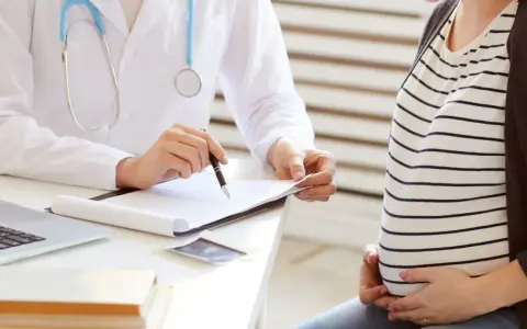 Lekarz omawia z ciężarną pacjentką kolejne trymestry ciąży, notując coś na dokumentach.
