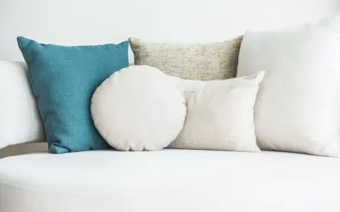 Cuscini di varie forme e colori su un divano bianco. Scopri come lavare i cuscini del divano per mantenerli freschi e puliti.
