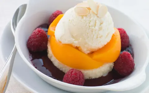 Ein köstlicher Pfirsich Melba: Vanilleeis auf Pfirsichspalten, umgeben von Himbeeren und dunkler Sauce, garniert mit Mandelblättchen.