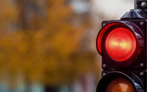 Close-up of a red traffic light with a blurred background of autumn foliage.
