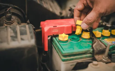 A hand removes a yellow cap from a truck battery, hinting at maintenance to ensure it lasts as long as possible.