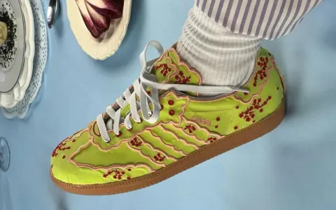 Jaskrawozielone buty Adidas z haftowanymi kwiatami wiśni i różowymi lamówkami, prawdopodobnie najdroższe buty Adidas, prezentowane na błękitnym tle.