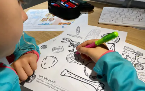 Dziecko koloruje edukacyjne karty pracy z dinozaurem i artefaktami.