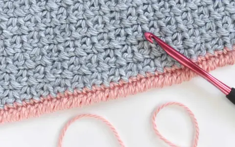 Detalle de tejido a crochet con punto cangrejo en rosa y gris. Una aguja rosa está lista para continuar el trabajo.