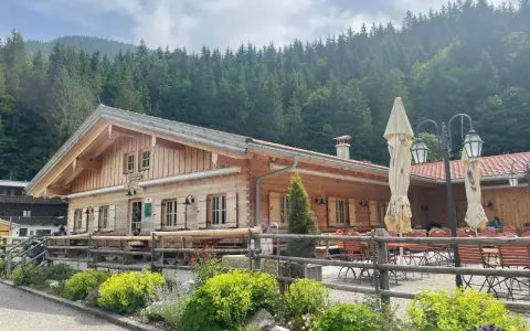 Holzhütte mit Biergarten und blühenden Blumen vor einer Bergkulisse. Die untere Firstalm lädt zum Verweilen ein.