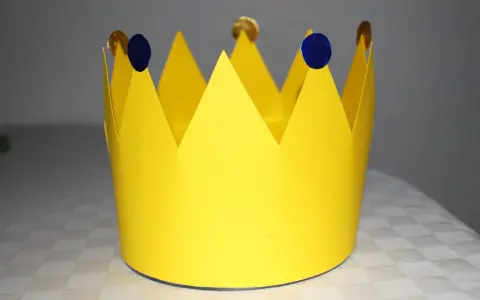 Gelbe Papierkrone, die zum **krone basteln** einlädt. Mit blauen Tupfern und goldenen Münzen verziert, wartet sie auf ihren kleinen König oder ihre kleine Königin.