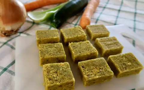 Cubetti di dado vegetale fatto in casa, pronti per insaporire le tue ricette. Sullo sfondo, ingredienti freschi come carote, zucchine e cipolla.