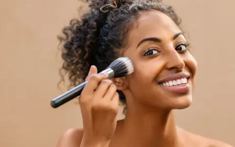 Donna sorridente applica il fondotinta con un pennello. La sua pelle luminosa è il risultato di cosmetici nichel free.