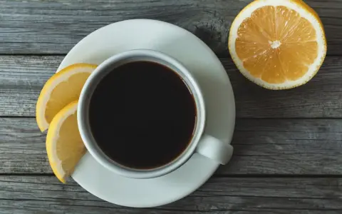 Eine Tasse schwarzer Kaffee mit Zitrone und Zitronenscheiben auf einem Holztisch.