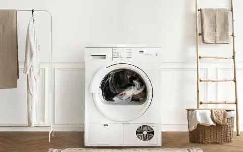 Vit torktumlare med kläder i trumman. Bredvid hänger en vit morgonrock och en beige filt. En trästege med en handduk står vid en korg med tvätt. Akryl textil i korgen.