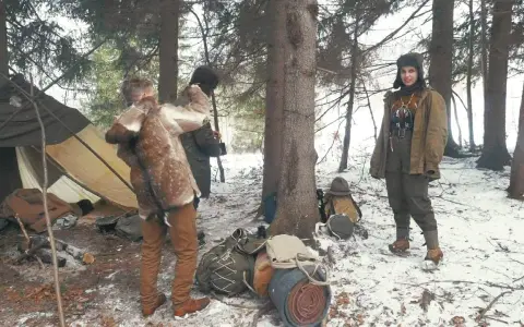 Zimowy obóz bushcraftowy. Dwie osoby w strojach z epoki, namiot, plecaki i sprzęt survivalowy.