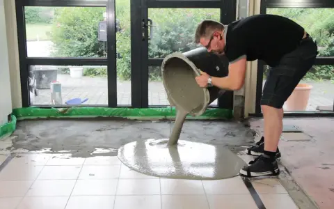 Mann gießt ausgleichsmasse auf fliesen. Der Boden wird nivelliert.