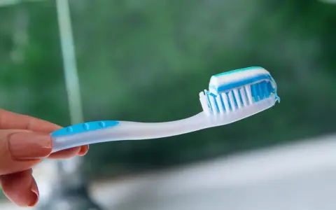 Dłoń trzymająca szczoteczkę z biało-niebieską pastą. Idealna jaka pasta po wybielaniu zębów dla lśniącego uśmiechu.