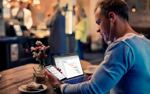Hombre revisa datos de business intelligence hostelería en su laptop y móvil, sentado en una cafetería.