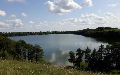 Spokojne jezioro Hańcza otoczone zielonymi lasami, z białymi chmurami na błękitnym niebie.