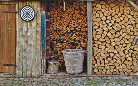 Drewno do kominka, starannie ułożone w drewutni. Obok kosz i pień, gotowe do pracy.