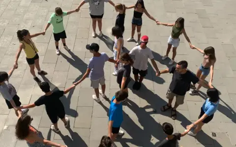 Un grupo de adolescentes participa en juegos cooperativos, tomados de la mano en un círculo en el exterior.