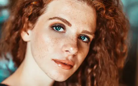 Primo piano di una ragazza con lentiggini e capelli rossi, con un trucco naturale che esalta la sua bellezza.