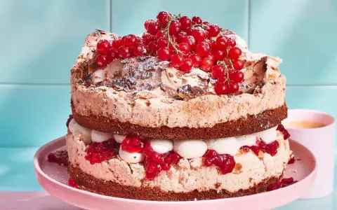 Ein zweistöckiger Johannisbeerkuchen mit Baiser, Sahne und roten Johannisbeeren, bestäubt mit Puderzucker und Mandelsplittern.