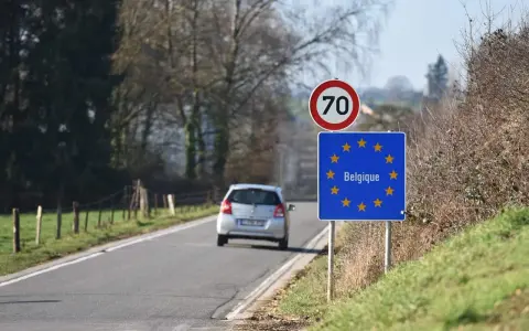 Znak graniczny Belgii, gdzie potrzebny paszport, na tle drogi i jadącego samochodu.
