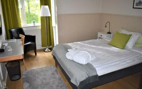Ett mysigt rum på Wendelsbergs Hotell & Vandrarhem med en bekväm säng, fåtölj och skrivbord.