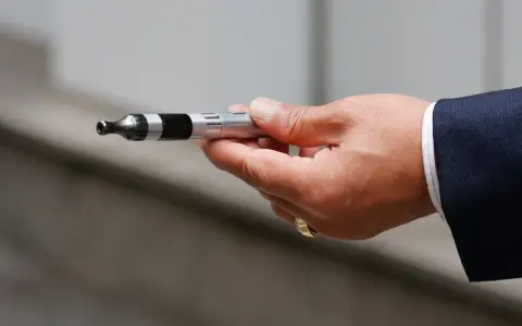 Mano con traje sosteniendo un cigarrillo electrónico, listo para vapear en el trabajo.