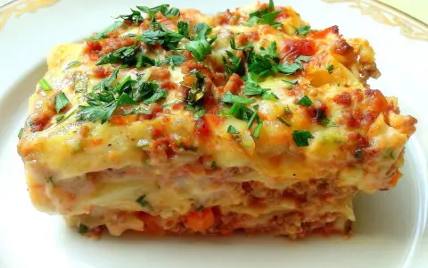 Pyszna lasagne Ani Starmach, z warstwami mięsa, sosu i sera, posypana świeżą natką pietruszki.