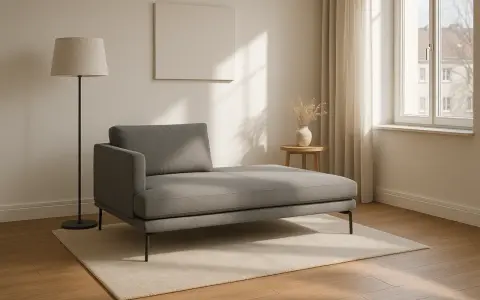 Chaise longue grigia moderna su tappeto chiaro, con lampada da terra e tavolino. Le misure sono perfette per un angolo relax.