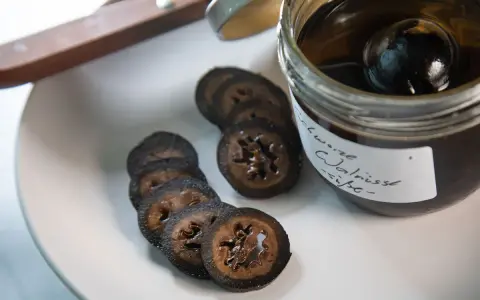 Schwarze Walnüsse in Sirup, bereit für ein köstliches schwarze walnuss rezept. Auf einem Teller liegen geschnittene Scheiben.