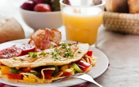 Pyszne śniadanie bez chleba: omlet z warzywami i serem, bekon, pomidory, truskawki i sok pomarańczowy.