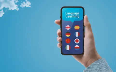 Dłoń trzyma smartfon z aplikacją do nauki języków. Wybór między Busuu czy Duolingo? Na ekranie flagi: UK, Hiszpanii, Niemiec, Francji, Chin, Japonii, Włoch, Polski.