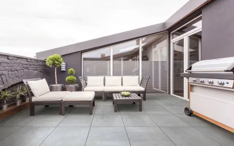 Terrasse moderne avec mobilier de jardin et barbecue. Le carrelage extérieur antidérapant est facile à nettoyer.
